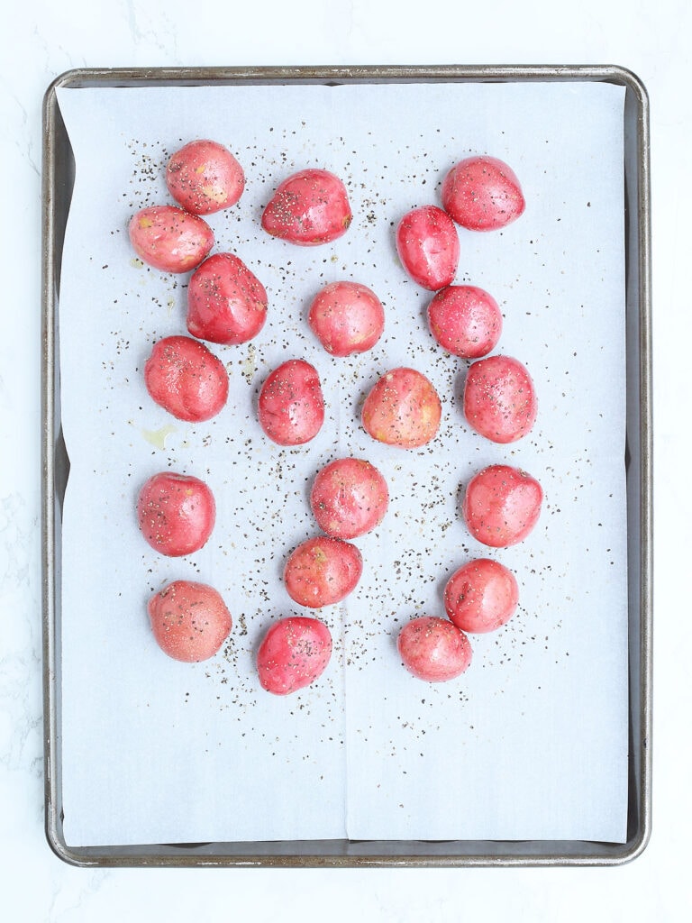 Whole red potatoes seasoned with olive oil, salt and pepper on a parchment paper lined baking sheet.