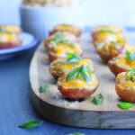 Spicy pimento cheese stuffed potato bites topped with sliced green onions on a wooden serving board.