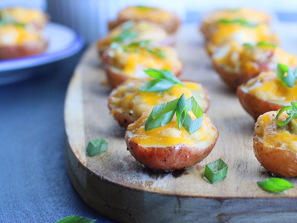 Spicy pimento cheese stuffed potato bites topped with sliced green onions on a wooden serving board.