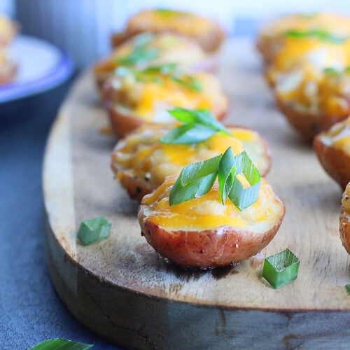Spicy pimento cheese stuffed potato bites topped with sliced green onions on a wooden serving board.