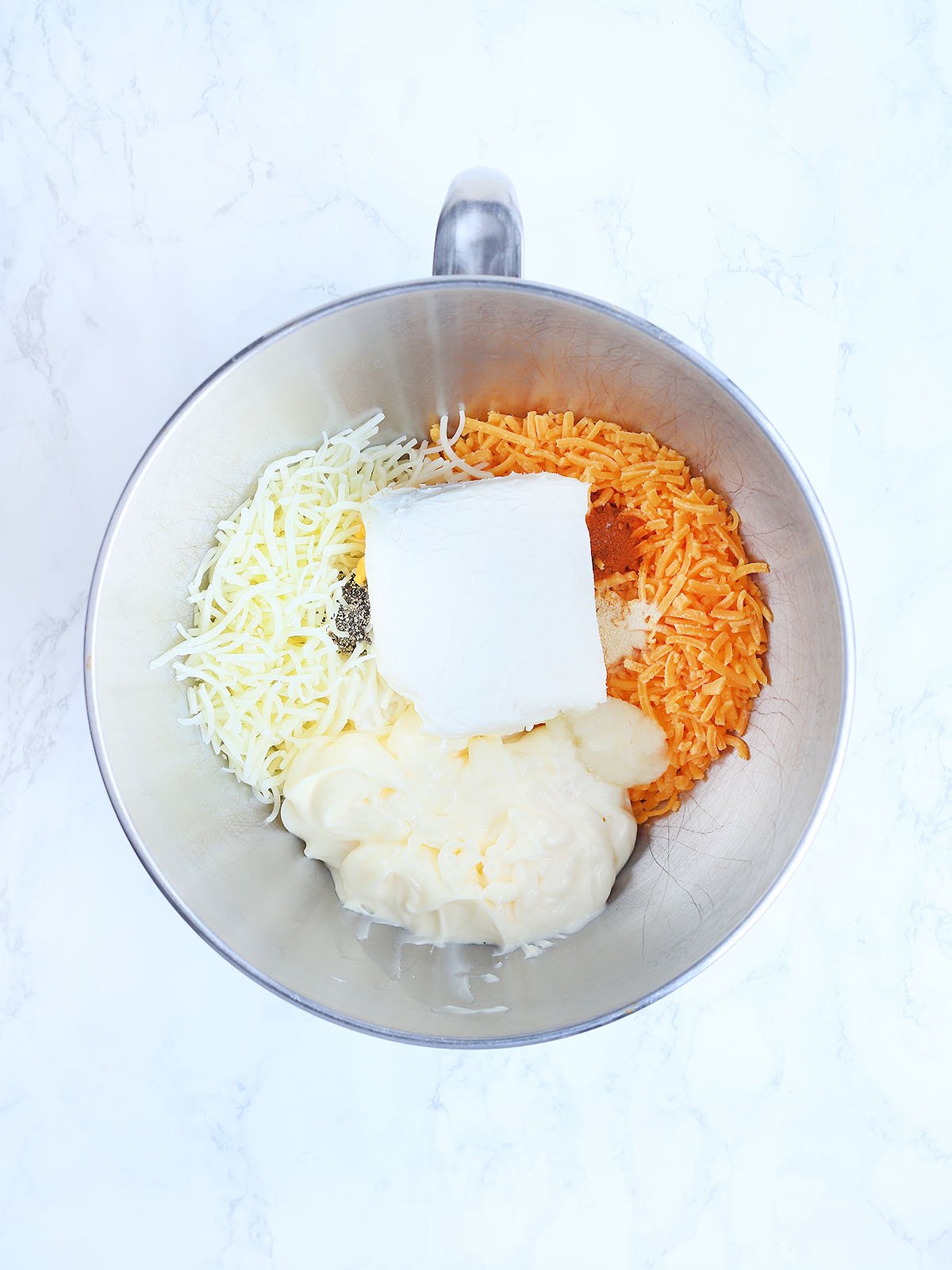 Cheese, mayonnaise, cream cheese and spices in a stainless steel mixing bowl.