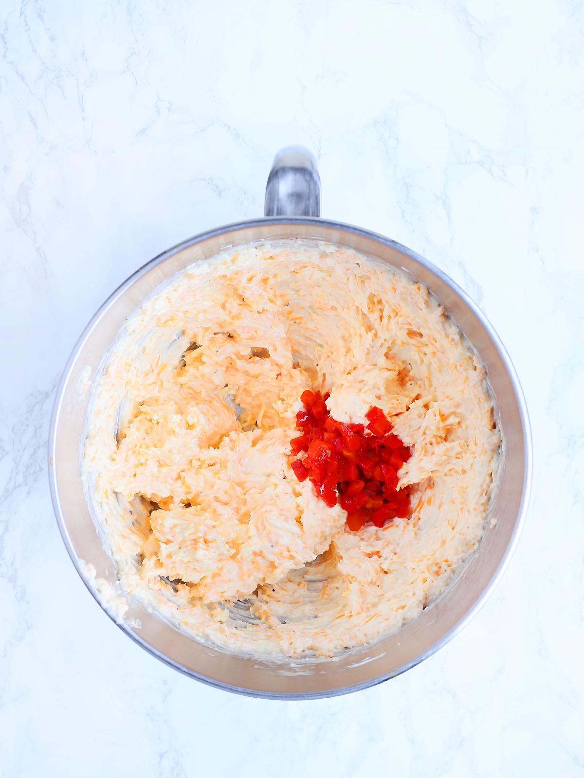 Adding the pimentos to the mixing bowl with the pimento cheese spread.