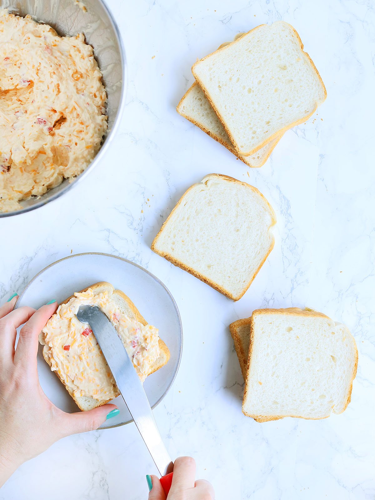 Hands spreading pimento cheese on slices of white bread.