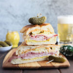 Two Cuban Reuben halves stacked on top of each other and garnished with a dill pickle.