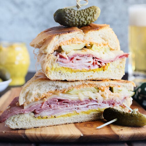 Two Cuban Reuben halves stacked on top of each other and garnished with a dill pickle.