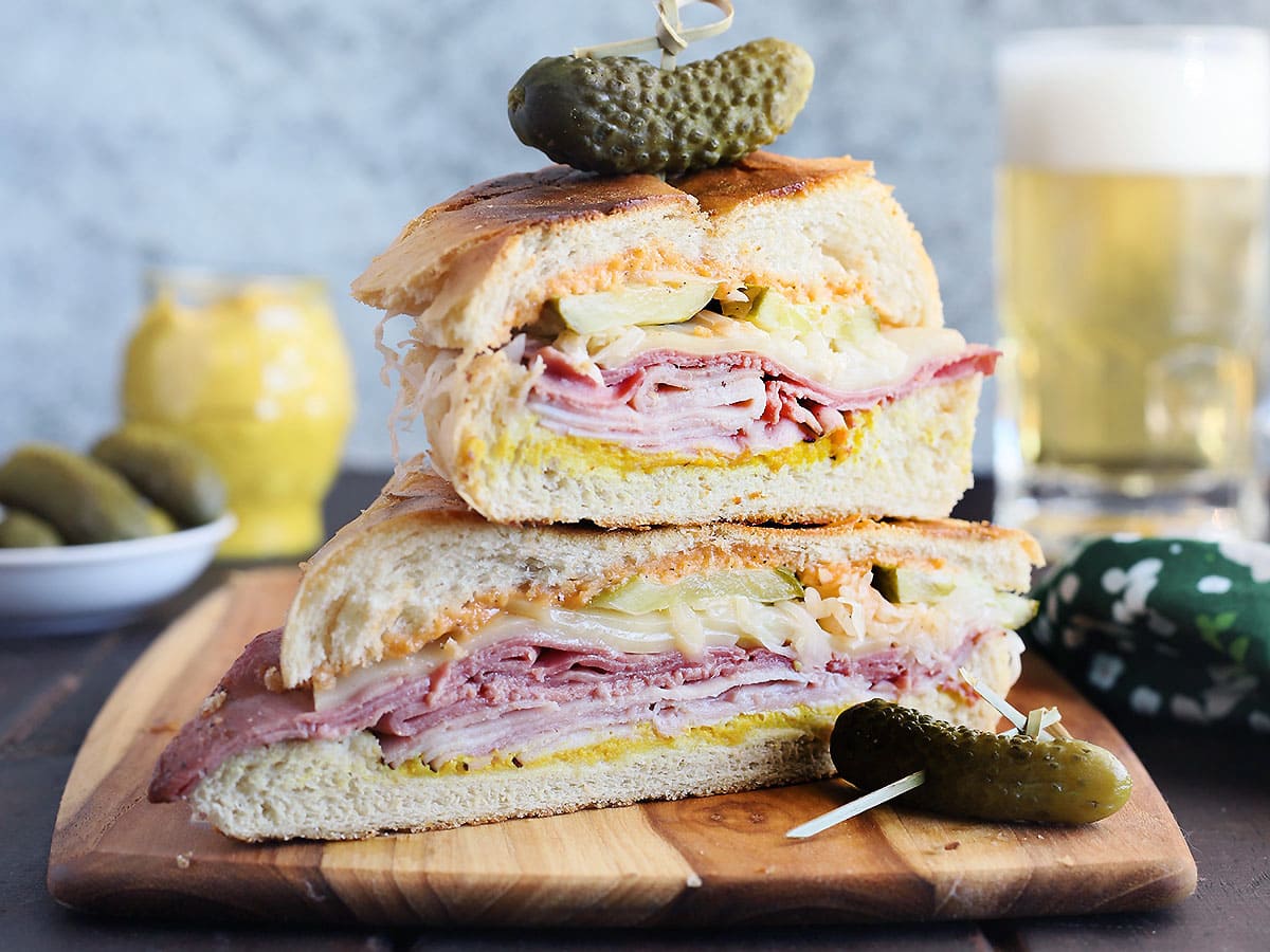 Two Cuban Reuben halves stacked on top of each other and garnished with a dill pickle.