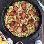 Southern fried cabbage and smoked sausage with bacon in a large cast iron Dutch oven with hot sauce and a basket of cornbread muffins on the side.