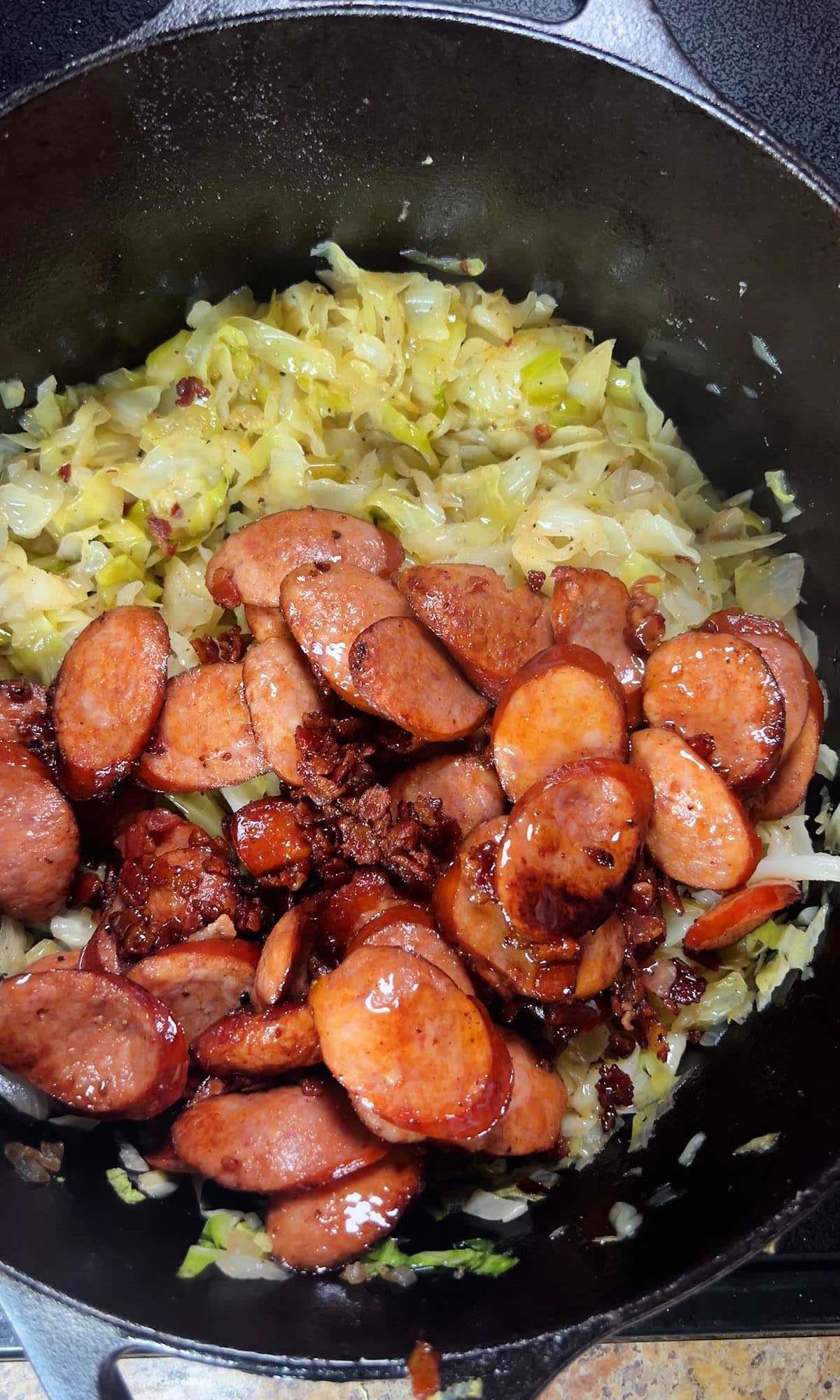 Adding the smoked sausage and bacon back to the pot of fried cabbage.