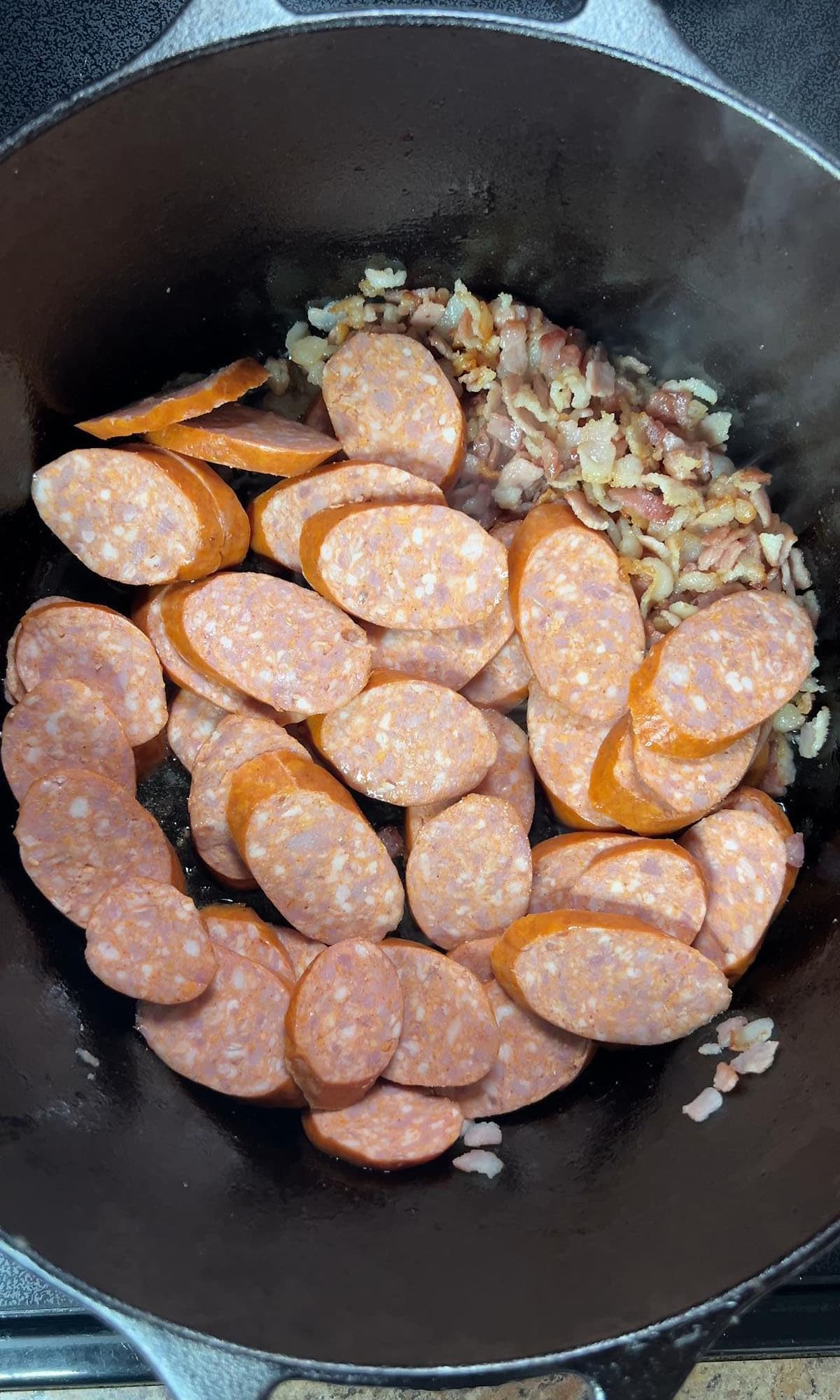 Adding the sausage to a Dutch oven with chopped bacon.