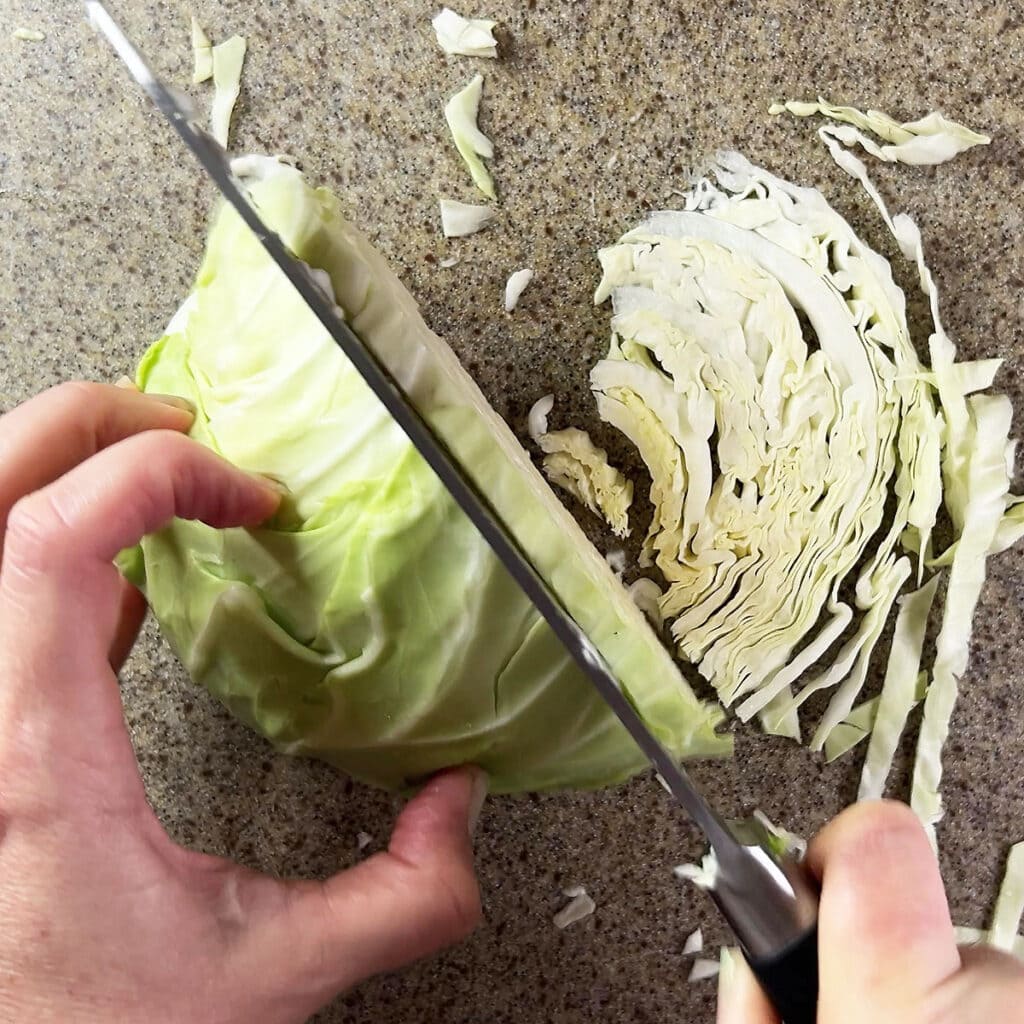 Hand using a knife to show how thick to cut the cabbage ribbons.