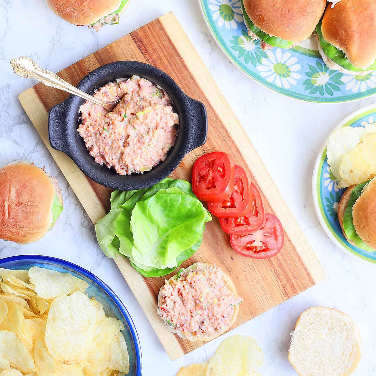 Old fashioned ham salad recipe in a small serving bowl on a cutting board with slider buns, lettuce and sliced tomatoes.