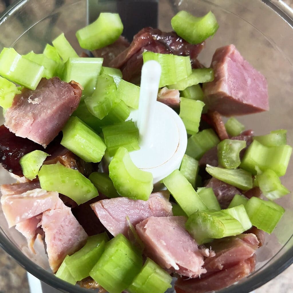 Chopped ham and celery for deviled ham in the bowl of a food processor.