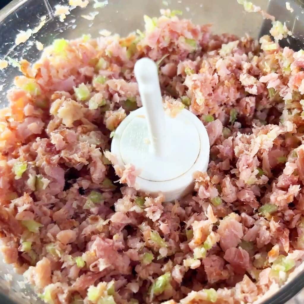 Finely diced ham and celery for a ham salad recipe in the bowl of a food processor.