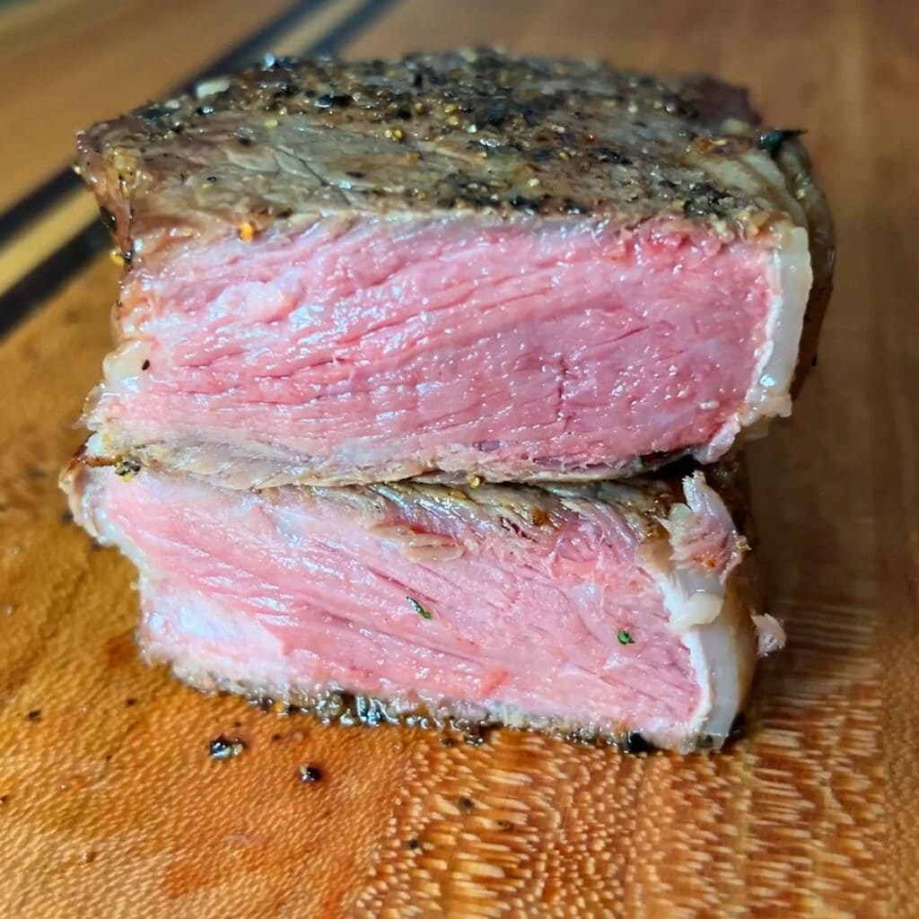 Cut of steak sliced in half on a cutting board to show a pink inside.