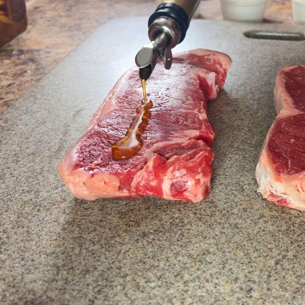 Pouring olive oil over the outside of a raw New York strip steak.