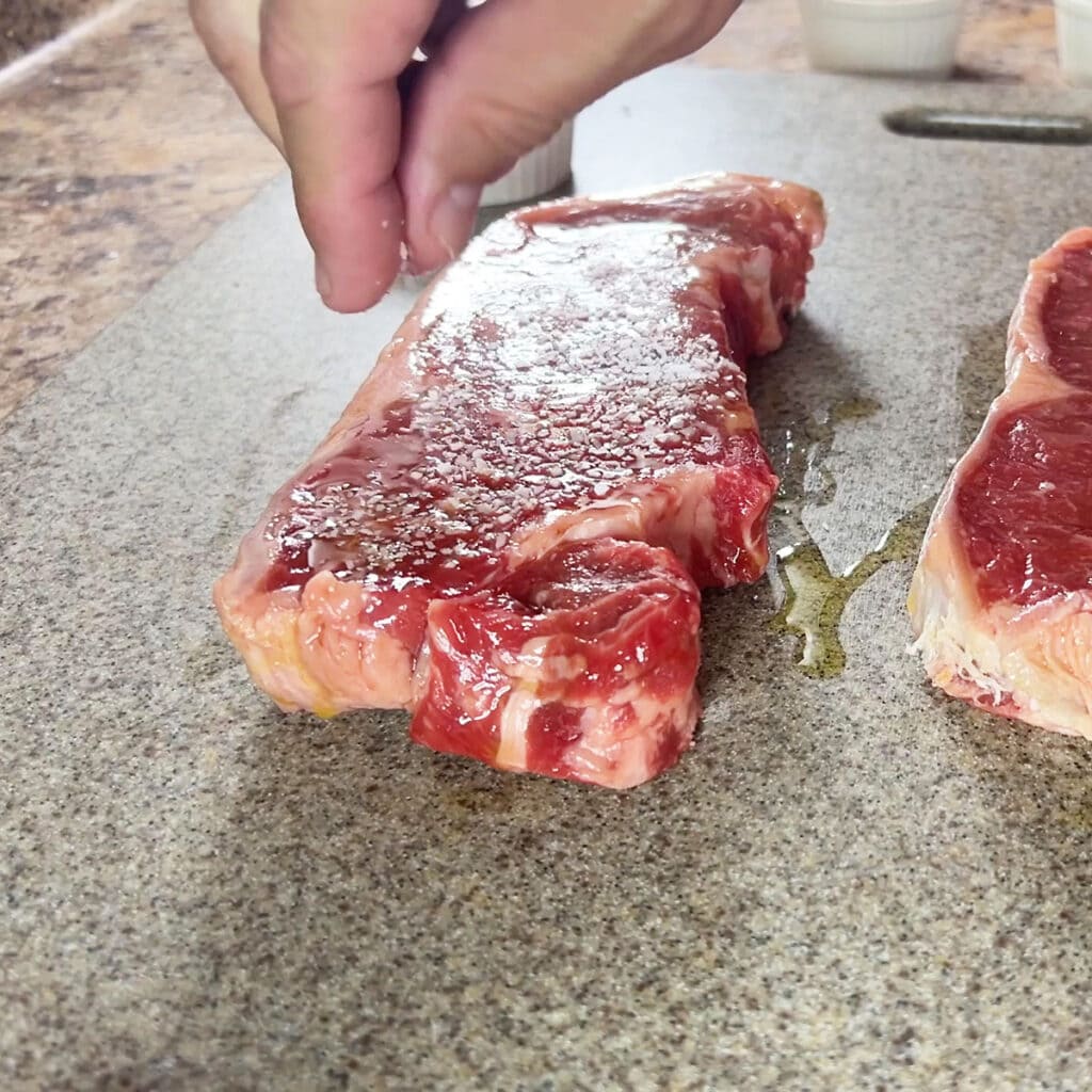Seasoning the steaks with kosher salt.