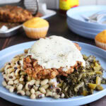 Chicken fried steak topped with country gravy on a plate with a pile of black-eyed peas and turnip greens.