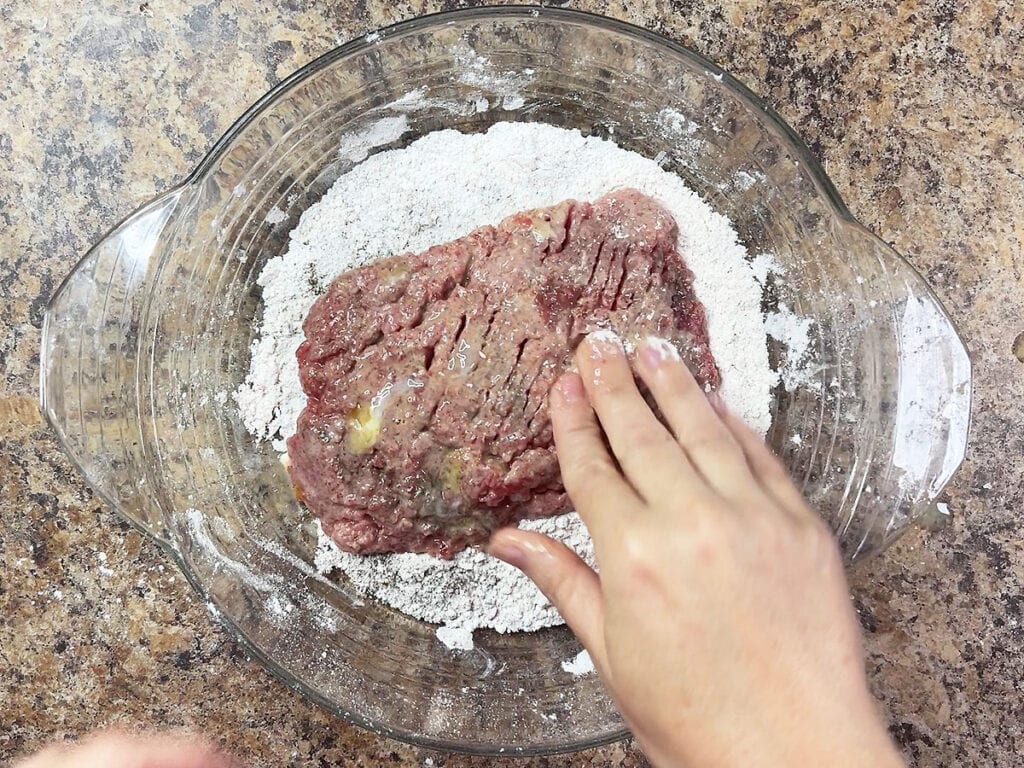 Giving the cubed steak a second coating in flour.