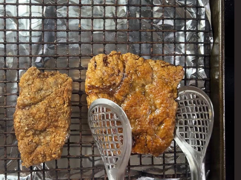 Removing cooked chicken fried steak to a wire rack lines with tin foil.