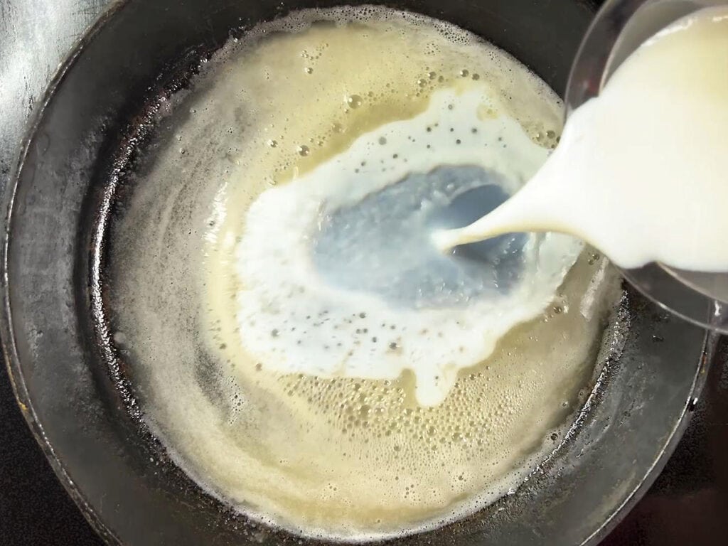 Adding milk into the skillet with the flour and oil.
