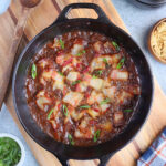 Smoked baked beans in a cast iron Dutch oven garnished with chopped cooked bacon and sliced green onions.