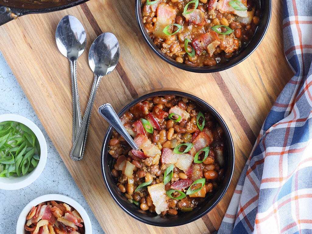 Individual bowls of baked beans garnished with chopped bacon and sliced green onions.
