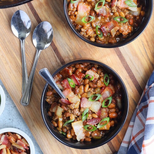 Individual bowls of baked beans garnished with chopped bacon and sliced green onions.