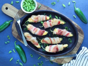 Cast iron plate with seven bacon wrapped jalapeno poppers garnished with sliced green onions.