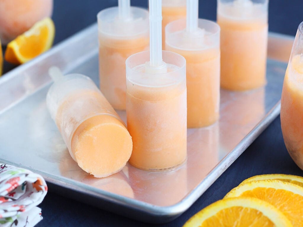 Six orange sherbet push up pops standing upright on a metal tray.