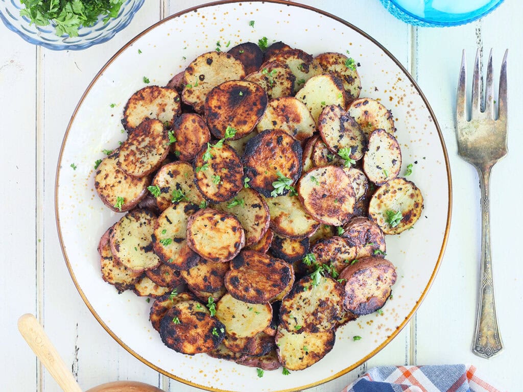 Serving plate of crispy fried Blackstone potatoes garnished with chopped parsley.