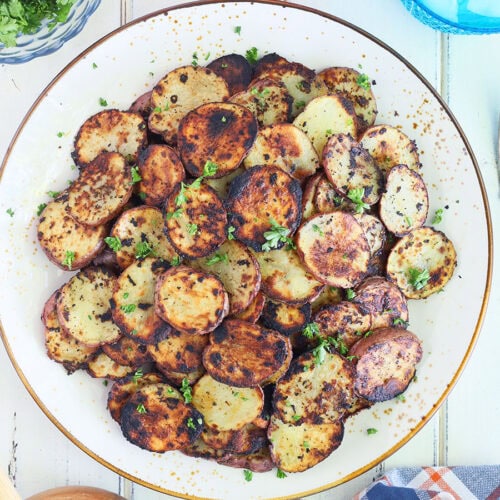 Serving plate of crispy fried Blackstone potatoes garnished with chopped parsley.