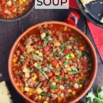 Pot of cowboy soup garnished with cilantro with two bowls of soup and a skillet of cornbread to the side.