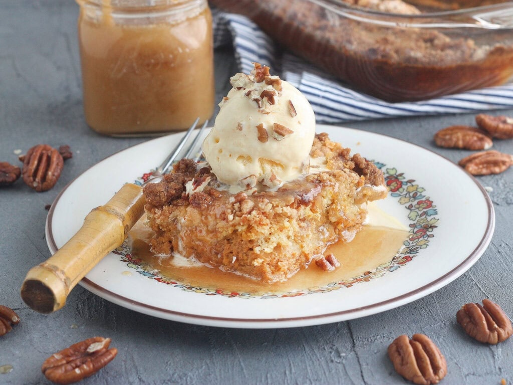 Slice of pumpkin crunch cake drizzled with caramel cause and topped with vanilla ice cream and chopped pecans.