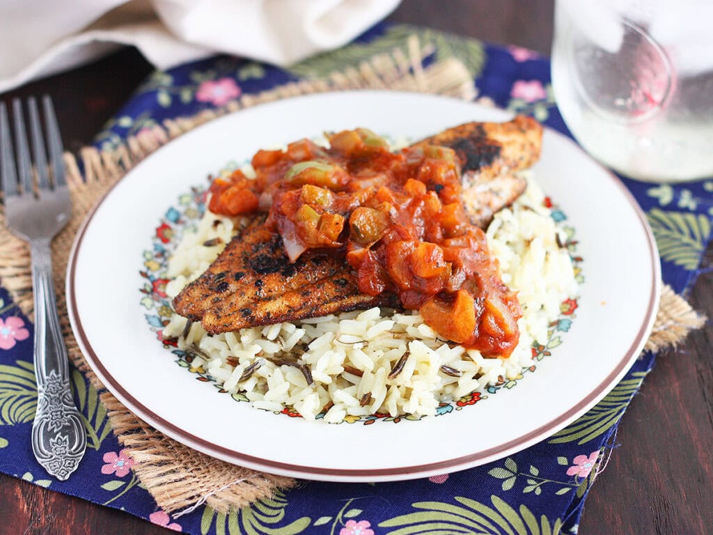 Blackened catfish fillet topped with Creole tomato sauce on a bed of rice.