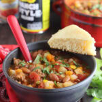 Bowl of cowboy soup garnished with chopped cilantro and a wedge of cornbread.