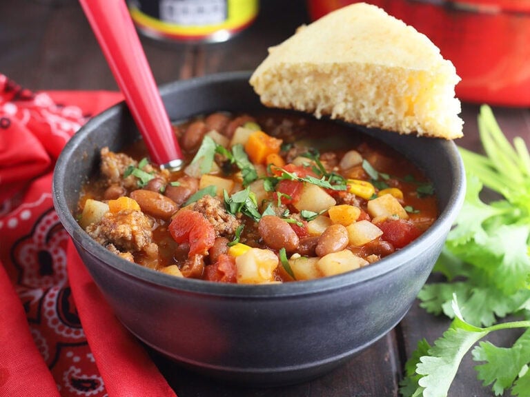 Bowl of cowboy soup garnished with chopped cilantro and a wedge of cornbread.