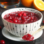 Bowl of bourbon cranberry sauce with a spoonful of cranberry sauce resting on a saucer.