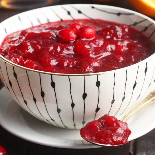 Bowl of bourbon cranberry sauce with a spoonful of cranberry sauce resting on a saucer.