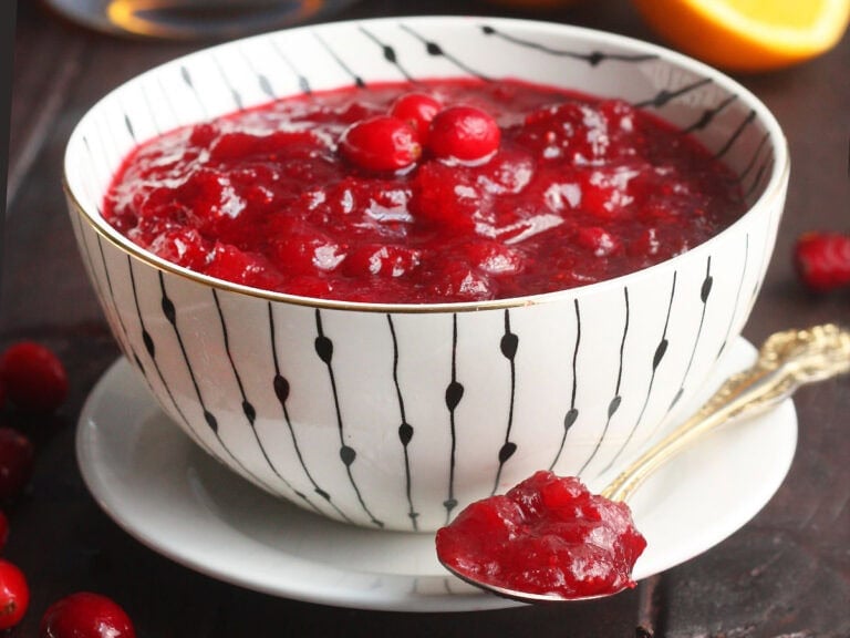 Bowl of bourbon cranberry sauce with a spoonful of cranberry sauce resting on a saucer.