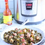 Serving dish full of collard greens with a bottle of hot sauce and an Instant Pot in the background.