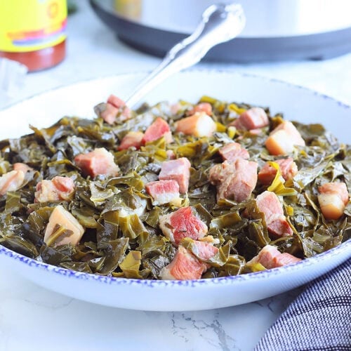 Serving dish full of collard greens with a bottle of hot sauce and an Instant Pot in the background.