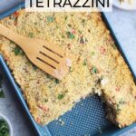 Wooden spatula laying on top of a pan of turkey tetrazzini. Two servings of tetrazzini are on plates to the side with small dishes of parsley and Parmesan cheese.