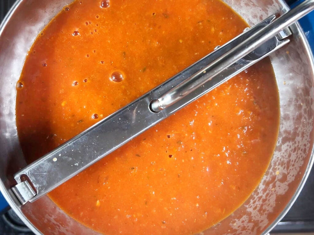 Tomato basil puree poured into the top of a hand crank food mill.