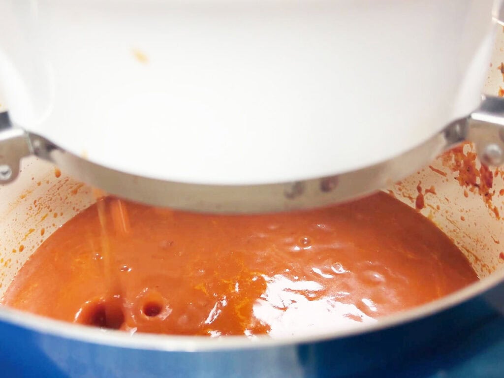 Tomato puree dripping out the bottom of a food mill into a stock pot.