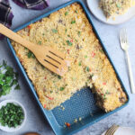Wooden spatula laying on top of a pan of turkey tetrazzini. Two servings have been removed and are sitting on plates to the side.