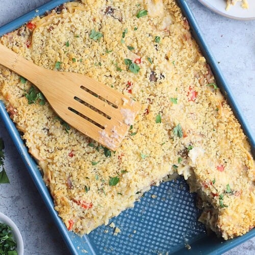 Wooden spatula laying on top of a pan of turkey tetrazzini. Two servings have been removed and are sitting on plates to the side.