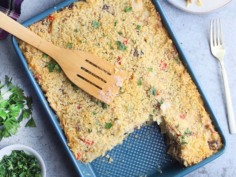 Wooden spatula laying on top of a pan of turkey tetrazzini. Two servings have been removed and are sitting on plates to the side.