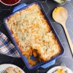 Savory sweet potato casserole with a serving removed. Cranberry sauce, green bean casserole, and a platter of sliced turkey on the side.