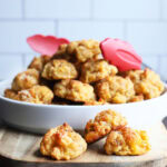 Three sausage balls on a serving board with a serving bowl of sausage balls in the background.