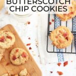 Four bacon and butterscotch chip cookies on a small cutting board, with additional cookies on a cooling rack, a glass of milk and a wooden spatula on the side.